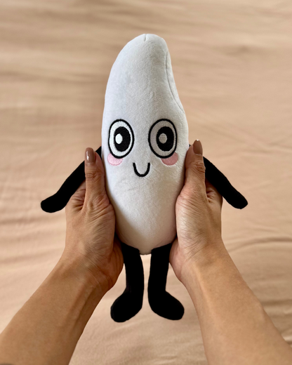 Person holding a plush toy shaped like a grain of rice with a face on a beige surface