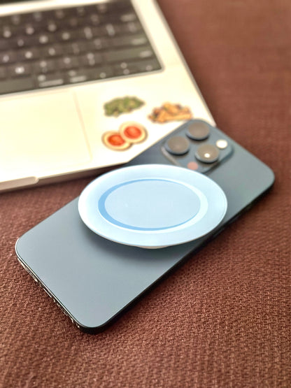 Phone with a pop socket on a brown surface, with a laptop in the background.