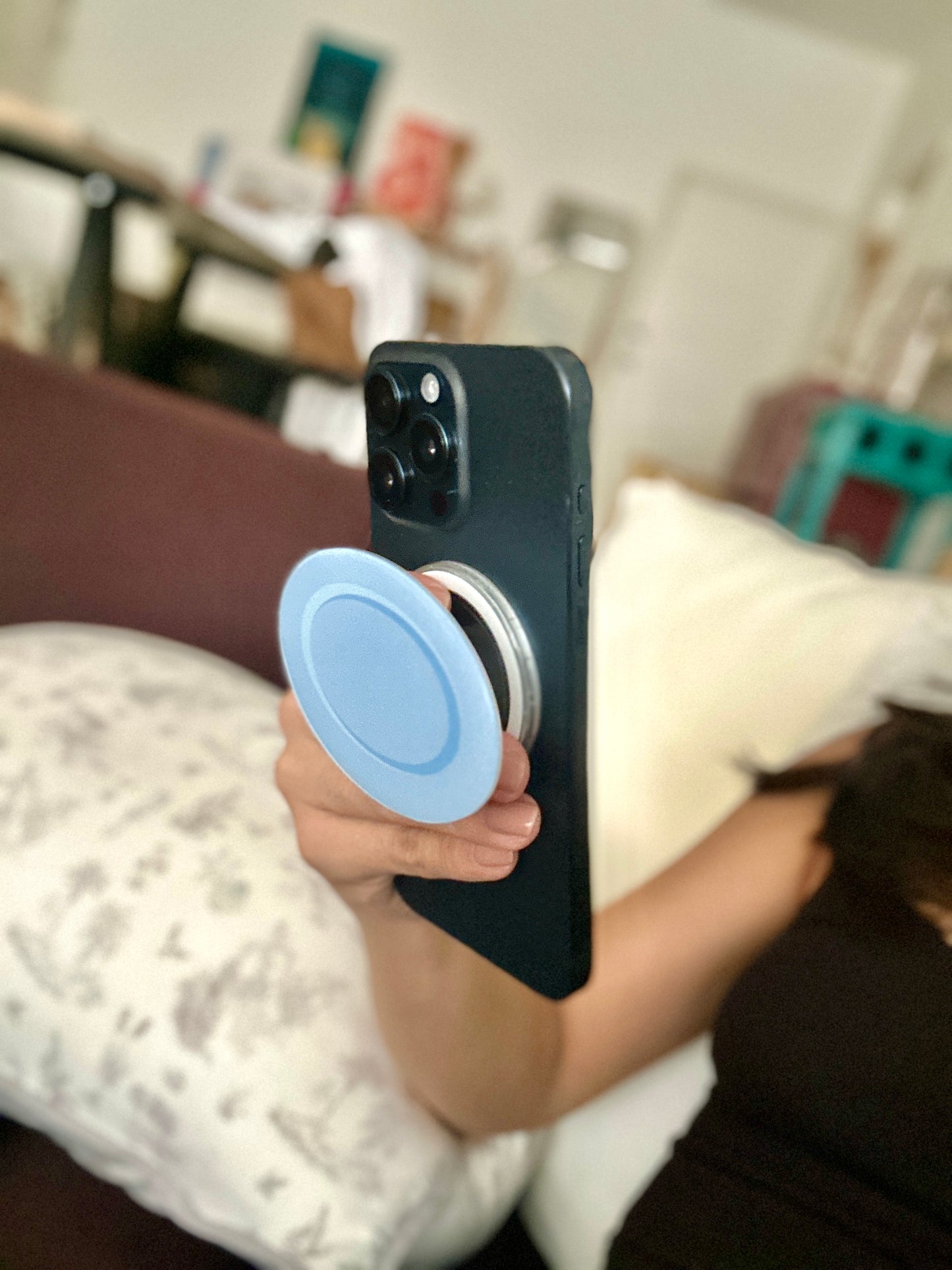 Person holding a phone with a blue kopitiam plate pop socket in an indoor setting